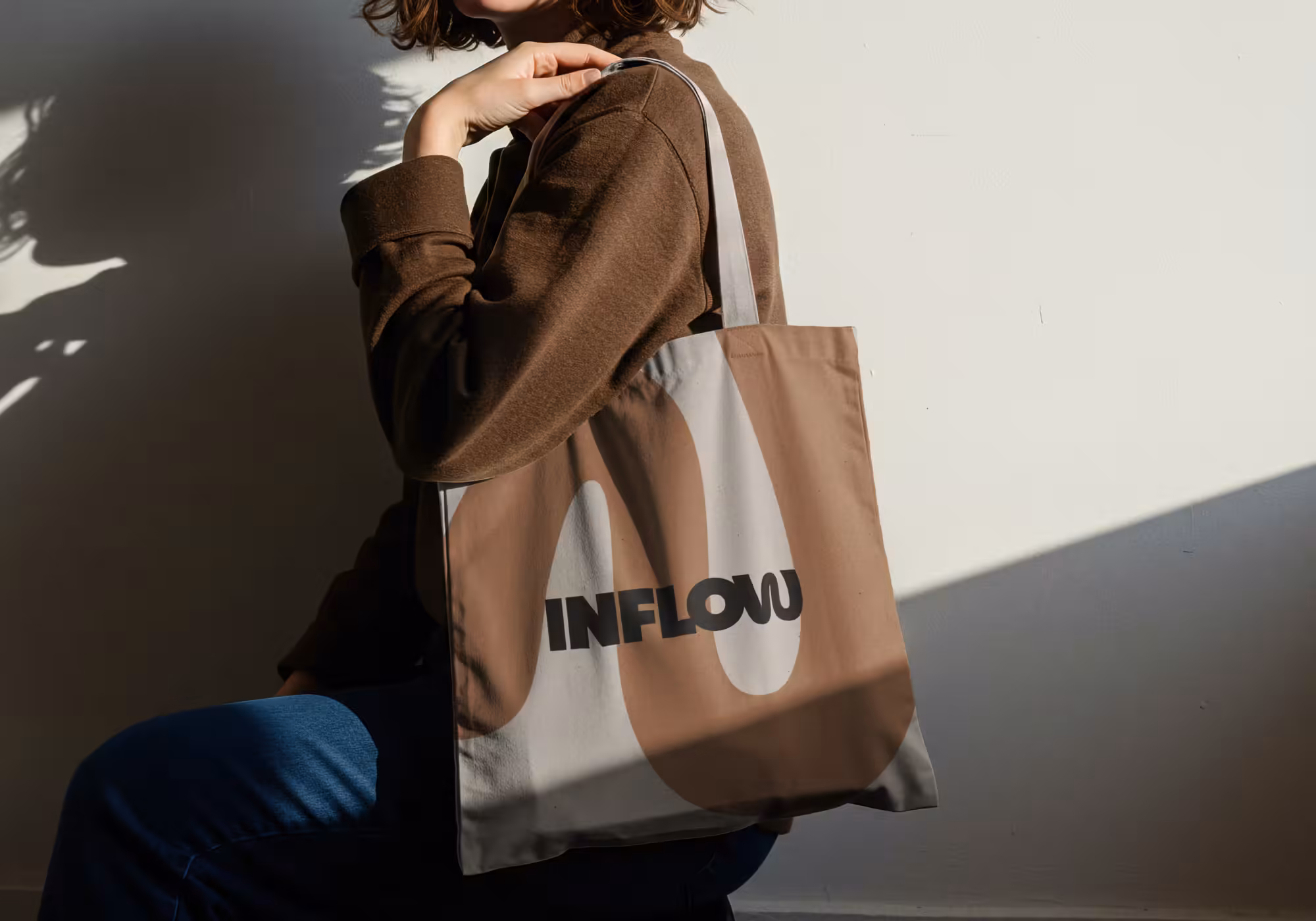 Person mit beiger Stofftasche mit Markenlogo im Sonnenlicht