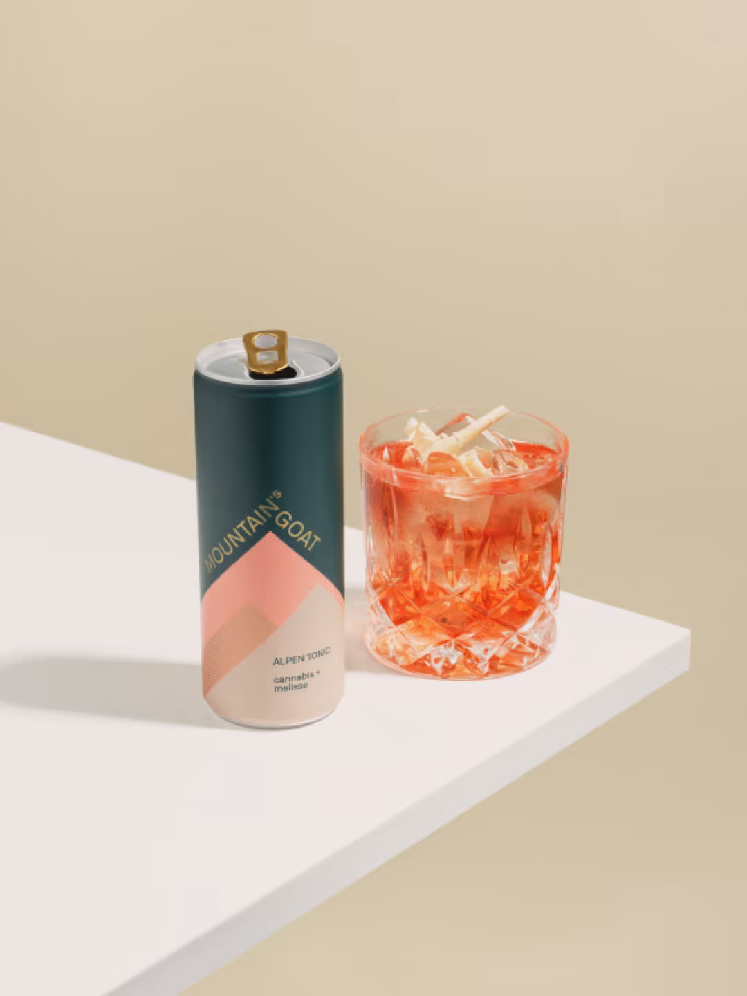 Dose Mountain's Goat neben einem Glas mit rosa Drink auf einem weißen Tisch vor beigem Hintergrund