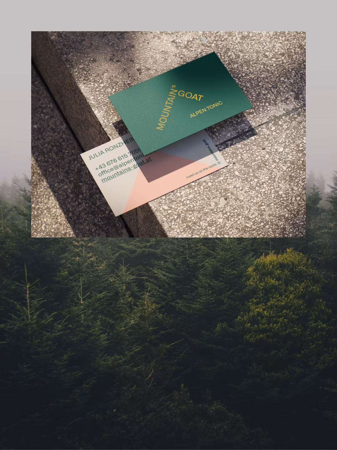 Grüne Visitenkarte von Mountain's Goat und eine rosa-weiße Karte auf Kies vor einem Tannenwald