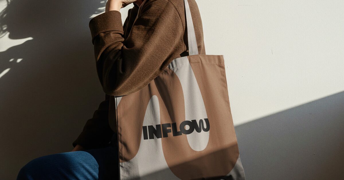 Person mit beiger Stofftasche mit Markenlogo im Sonnenlicht
