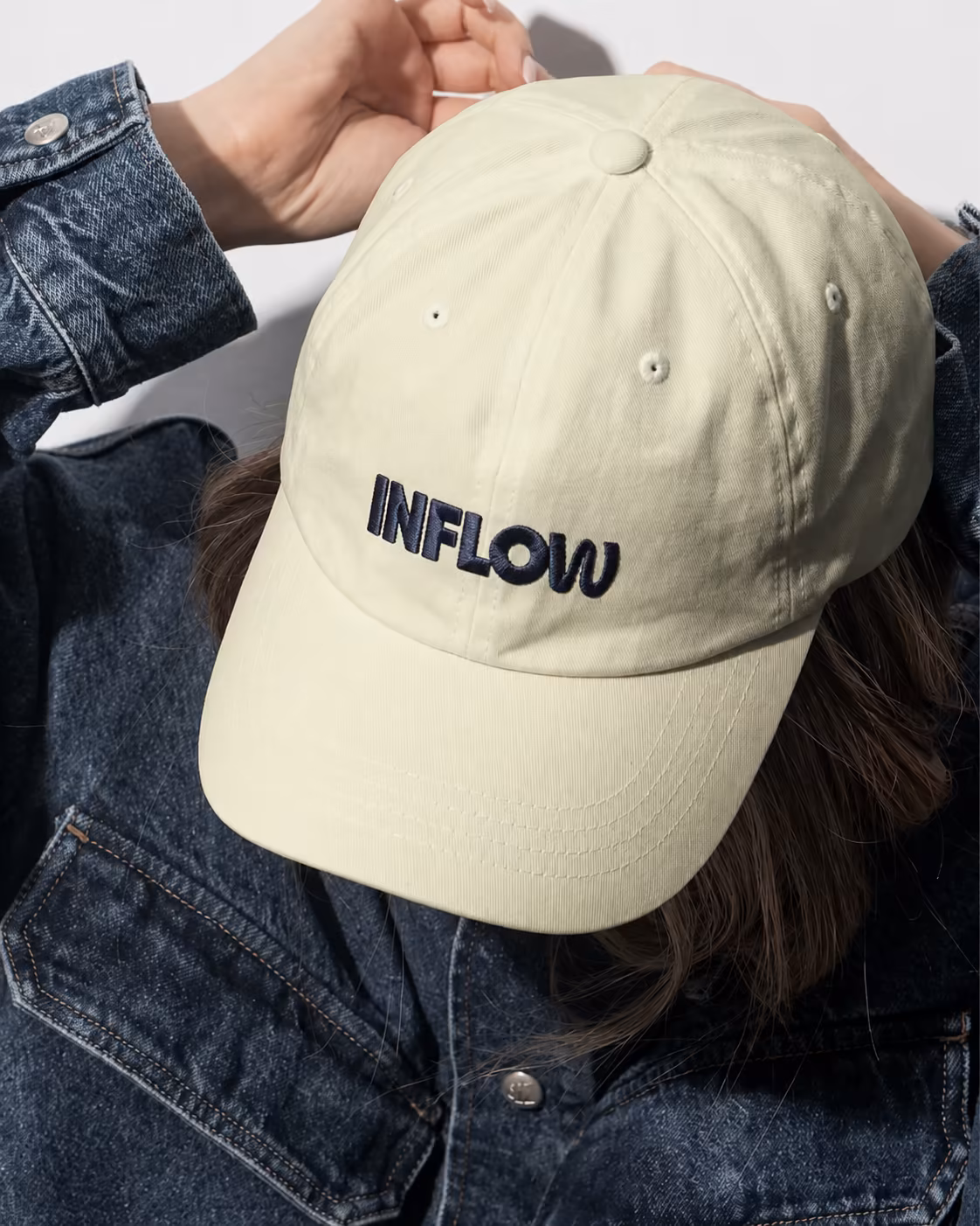 Person mit hellgrüner Cap mit INFLOW-Stickerei und Jeansjacke